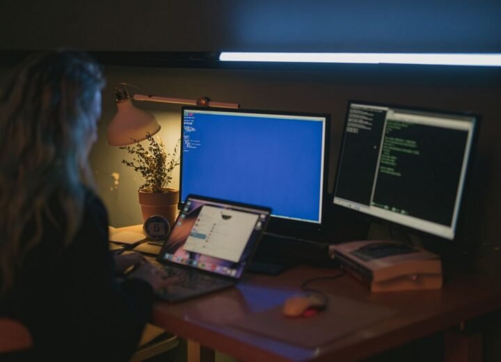 Person working at a dimly lit desk with monitors
