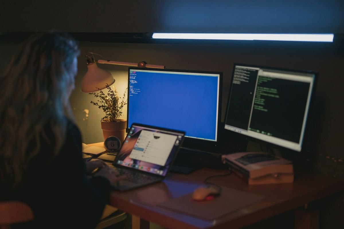 Person working at a dimly lit desk with monitors